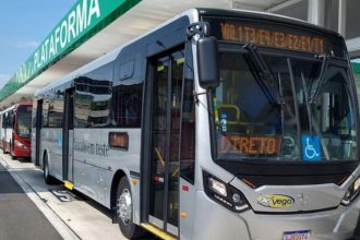 Ônibus estacionado em plataforma com letreiro indicando destino e inscrição "Veículo em teste".