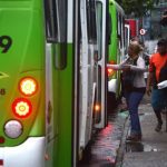 Ônibus verde 'Via Verde' com pessoas embarcando e desembarcando em uma rua movimentada para abordar sobre mudanças de linhas de ônibus