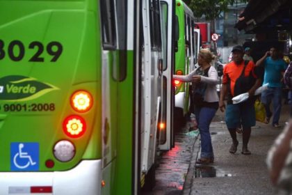 Ônibus verde 'Via Verde' com pessoas embarcando e desembarcando em uma rua movimentada para abordar sobre mudanças de linhas de ônibus