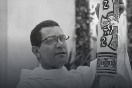 Padre Orlando Barbosa segurando uma vela cerimonial em preto e branco.