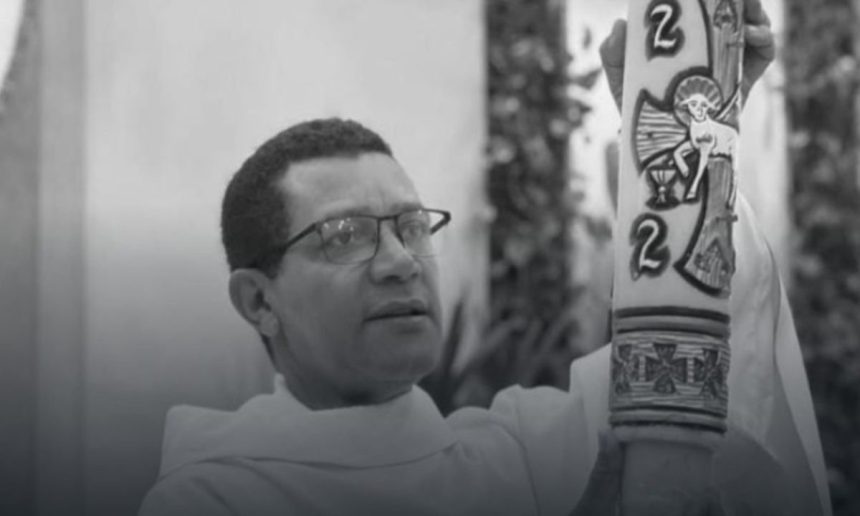 Padre Orlando Barbosa segurando uma vela cerimonial em preto e branco.