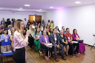 Palestrante em congresso de enfermagem oncológica, com público atento.