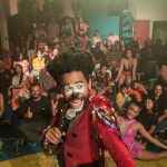 Palhaço se apresentando em um palco, com grande público ao fundo.