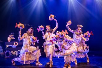 Performance teatral 'Buia Teatro' com figurinos extravagantes e máscaras de peixe.