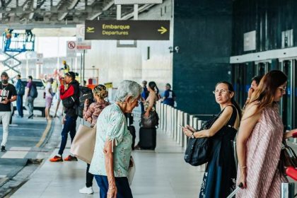 Pessoas em aeroporto, indicando embarque, com sinalização de 'Departure'.