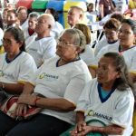 Pessoas em evento educacional, com foco em mulheres com óculos e camisetas com logo da Prefeitura de Manaus.