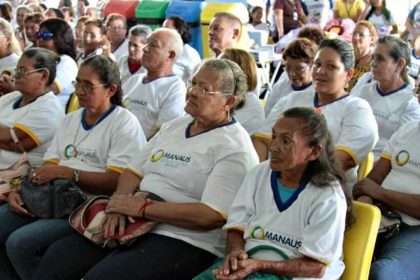 Pessoas em evento educacional, com foco em mulheres com óculos e camisetas com logo da Prefeitura de Manaus.