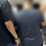 Pessoas em pé em uma sala, algumas com roupas escuras, outras com roupas claras.