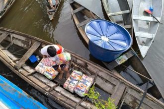 Pessoas transportando mantimentos em barcos de madeira em área alagada, possivelmente em vazante.