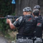 Policiais ROCAM em ação, com fuzil em punho, em local não especificado.