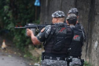 Policiais ROCAM em ação, com fuzil em punho, em local não especificado.