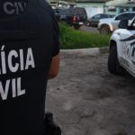 Policial civil em ação, com viatura da polÃcia no fundo.
