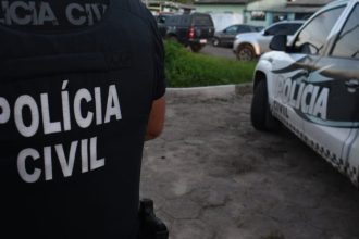 Policial civil em ação, com viatura da polícia no fundo.