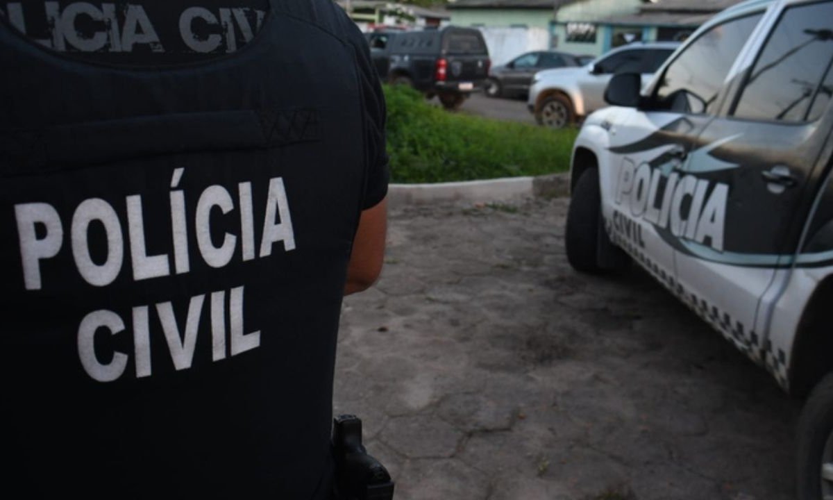 Policial civil em ação, com viatura da polícia no fundo.