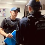 Policial conversa com colega em operação policial. Um deles usa colete e boné.