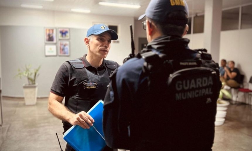 Policial conversa com colega em operação policial. Um deles usa colete e boné.