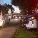 Policial em frente a viatura e ônibus, em celebração a segurança no transporte de trabalhadores em Manaus.
