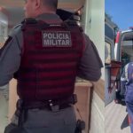 Policial militar em colete tático entra em uma clínica, ambulância estacionada do lado de fora.