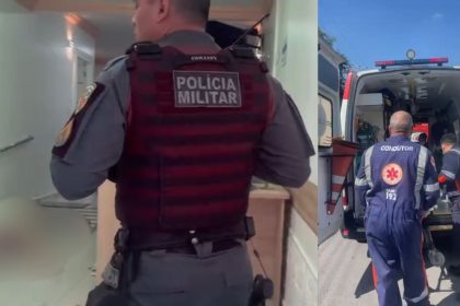 Policial militar em colete tático entra em uma clínica, ambulância estacionada do lado de fora.