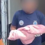 Policial segura bebê envolta em tecido rosa após achado de corpo.