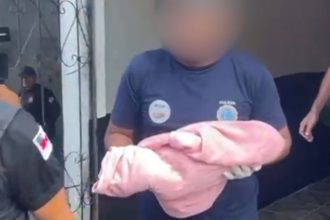 Policial segura bebê envolta em tecido rosa após achado de corpo.