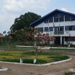 Prédio da prefeitura de Apuí, com jardim e céu azul.