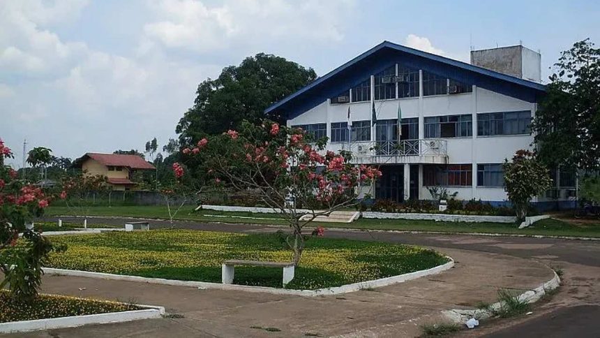 Prédio da prefeitura de Apuí, com jardim e céu azul.