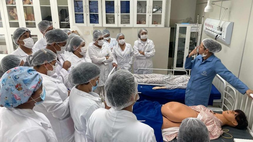 Professora de enfermagem demonstra em manequim para turma em sala de aula.