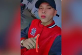 Rafael da Silva de Lima, procurado por homicídio, com jaqueta vermelha e boné preto.