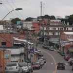 Rua em favela no Morro da Liberdadscom casas de tijolos e fios elétricos, carros e céu nublado.