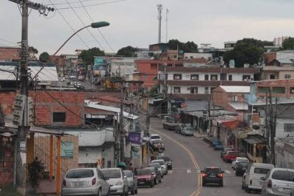 Rua em favela no Morro da Liberdadscom casas de tijolos e fios elétricos, carros e céu nublado.
