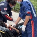 Socorristas atendem pessoa ferida em maca, perto de ambulância.