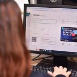 Tela de computador com inscrição Cetam para cursos de qualificação profissional, com pessoa usando o teclado.