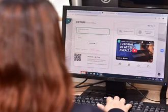 Tela de computador com inscrição Cetam para cursos de qualificação profissional, com pessoa usando o teclado.