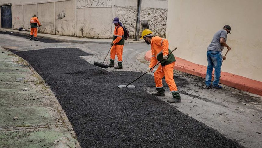 Trabalhadores asfaltando rua em Itapiranga, com uniforme laranja e ferramentas.