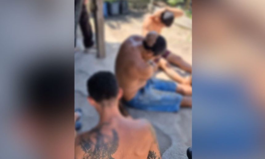 Três homens em ambiente externo, um com tatuagem nas costas. Imagem borrada.