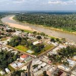 Vista aérea de cidade de Guajará à beira de rio, com mata densa ao fundo e construções urbanas.