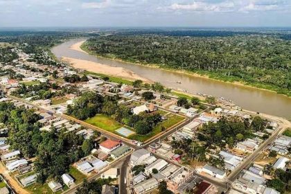 Vista aérea de cidade de Guajará à beira de rio, com mata densa ao fundo e construções urbanas.