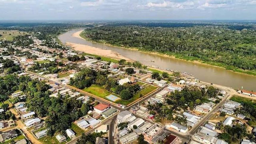 Vista aérea de cidade de Guajará à beira de rio, com mata densa ao fundo e construções urbanas.