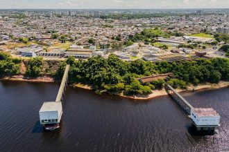 Vista aérea de estação de tratamento de água em Manaus, com cidade ao fundo e rio em primeiro plano.