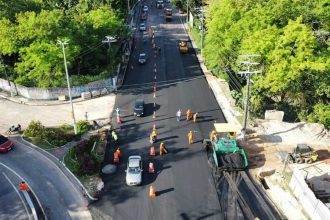 Vista aérea de obras de pavimentação na avenida Umberto Calderaro Filho em Manaus, com veículos e operários.