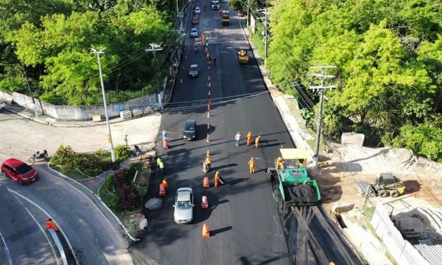 Vista aérea de obras de pavimentação na avenida Umberto Calderaro Filho em Manaus, com veículos e operários.