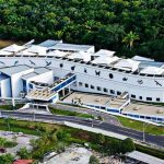 Vista aérea de um edifÃcio branco moderno com detalhes em azul, cercado por vegetação exuberante. Se trata do prédio do Centro de Biotecnologia da Amazônia (CBA).