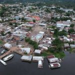 Vista aérea de uma cidade ribeirinha na Amazônia, com casas, barcos e rio. Manaquirii