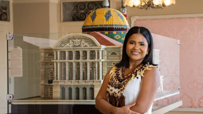 Advogada amazonense sorrindo ao lado de réplica de prédio