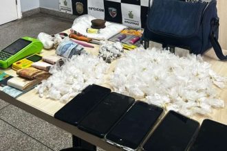 Apreensão de drogas e objetos em uma mesa, incluindo celulares, dinheiro e embalagens de entorpecentes.
