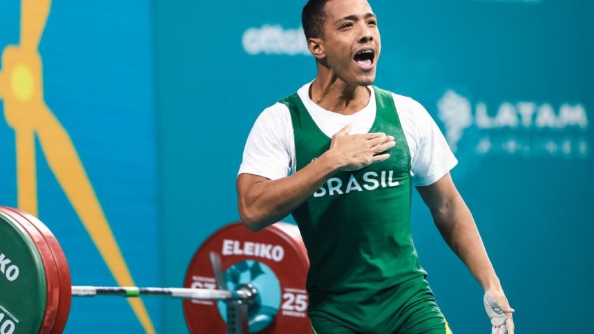 Atleta brasileiro comemorando vitória no levantamento de peso, vestindo uniforme do Brasil.