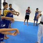 Aula de jiu-jítsu com crianças, ministrada por um professor em ambiente interno.