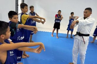 Aula de jiu-jítsu com crianças, ministrada por um professor em ambiente interno.