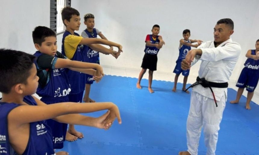 Aula de jiu-jítsu com crianças, ministrada por um professor em ambiente interno.